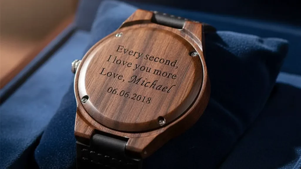 A close-up macro shot of a personalized wooden watch, shown face down on a soft cushion to reveal a custom romantic engraving on the back, symbolizing a 5th-year wood anniversary gift.
